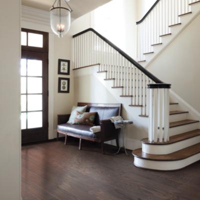 dark hardwood flooring in entryway with staircase and dark brown leather couch.